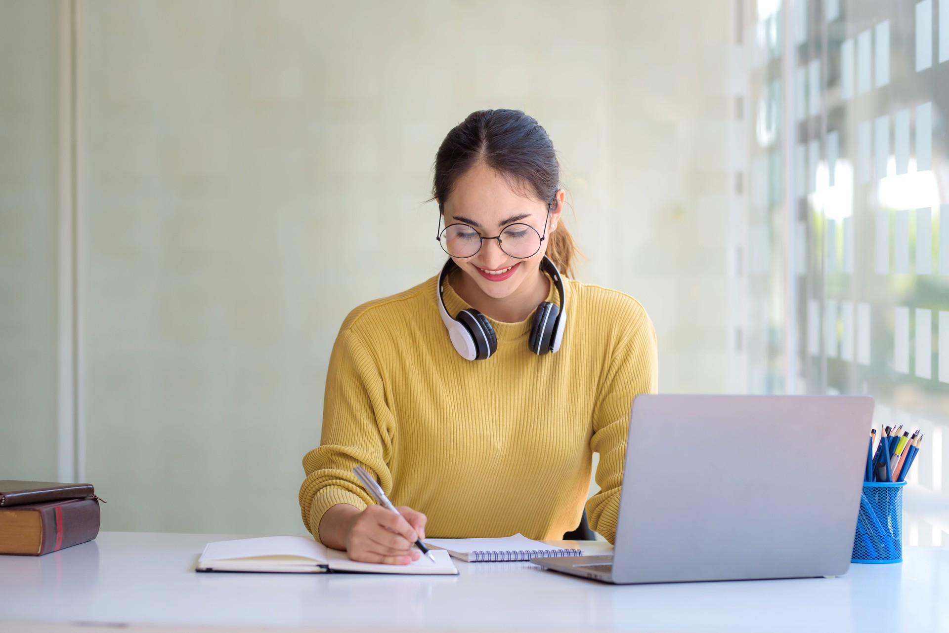 Happy young Asian student woman wearing headphones looking at webcam, looking at camera, during virtual meeting or video call talk.